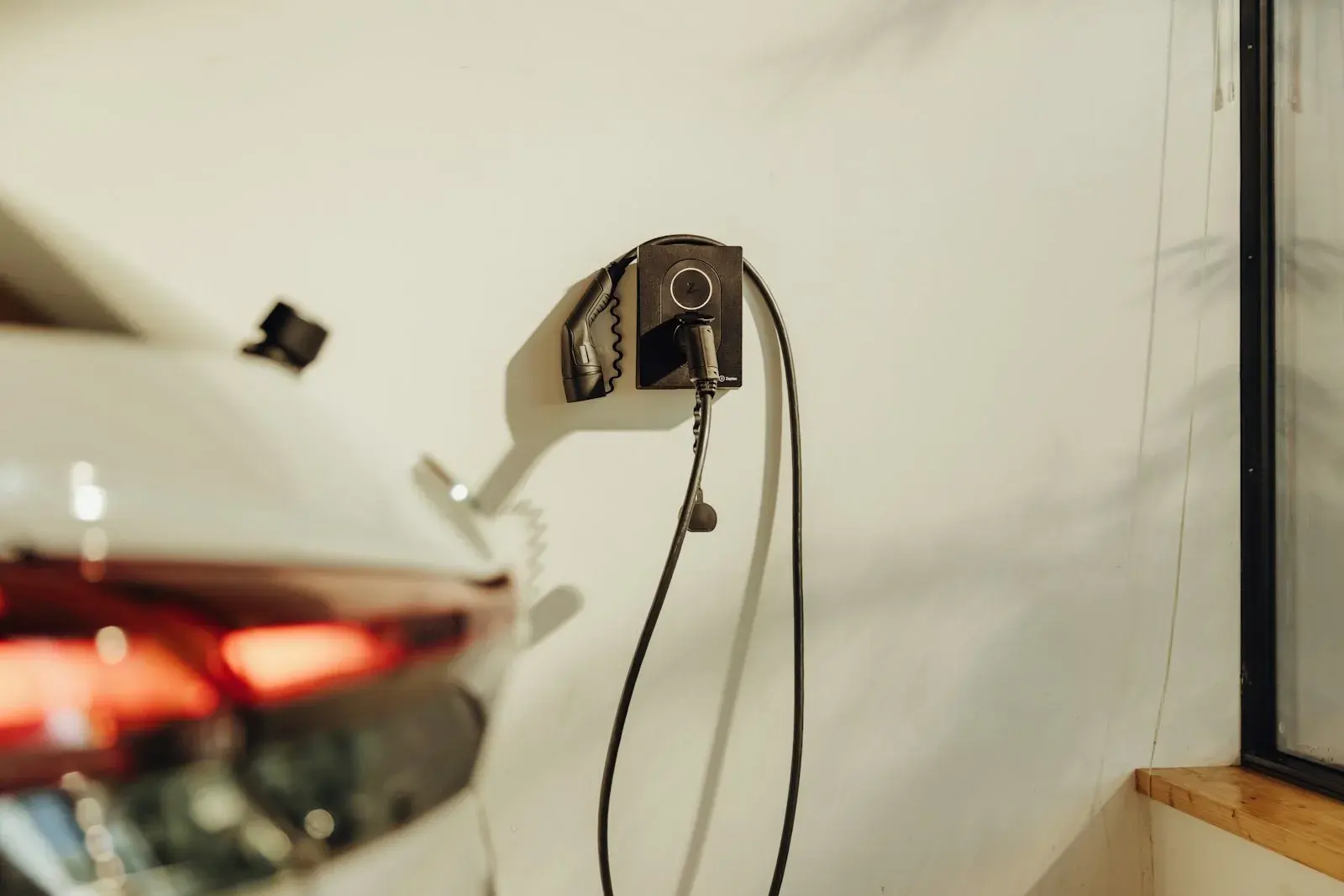 Veggmontert elbillader med ladekabel koblet til en bil i carport